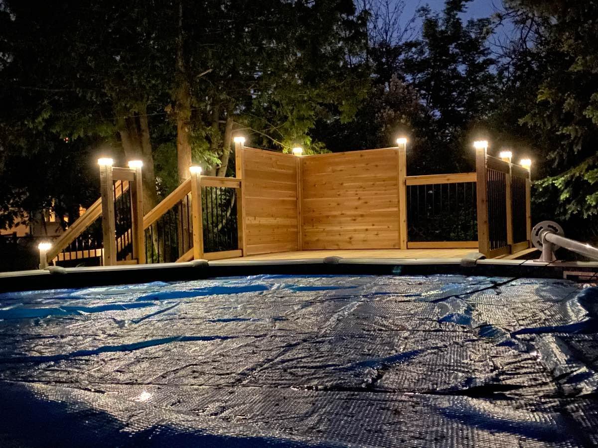 Lit cedar deck with a privacy screen at twilight beside a pool