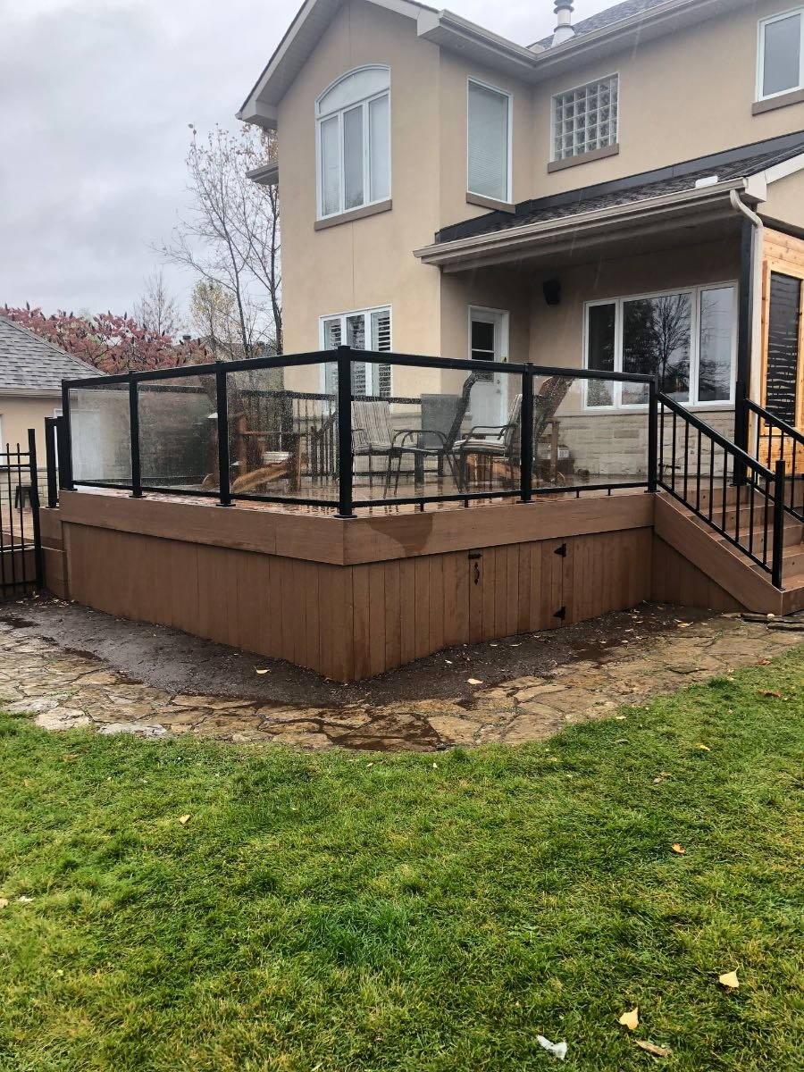 Raised deck with a black-framed glass railing behind a stucco home