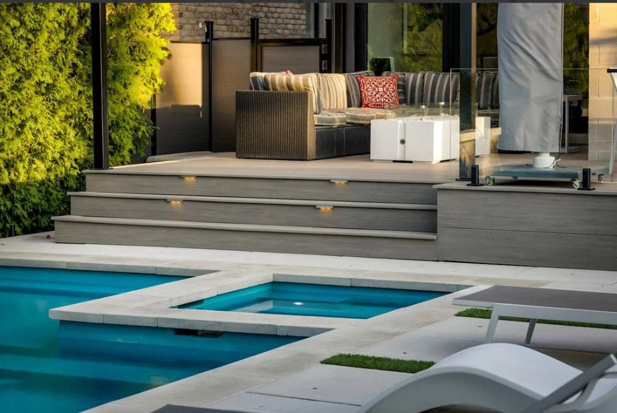 Grey composite deck with a built-in hot tub, lit steps and lounge furniture at dusk