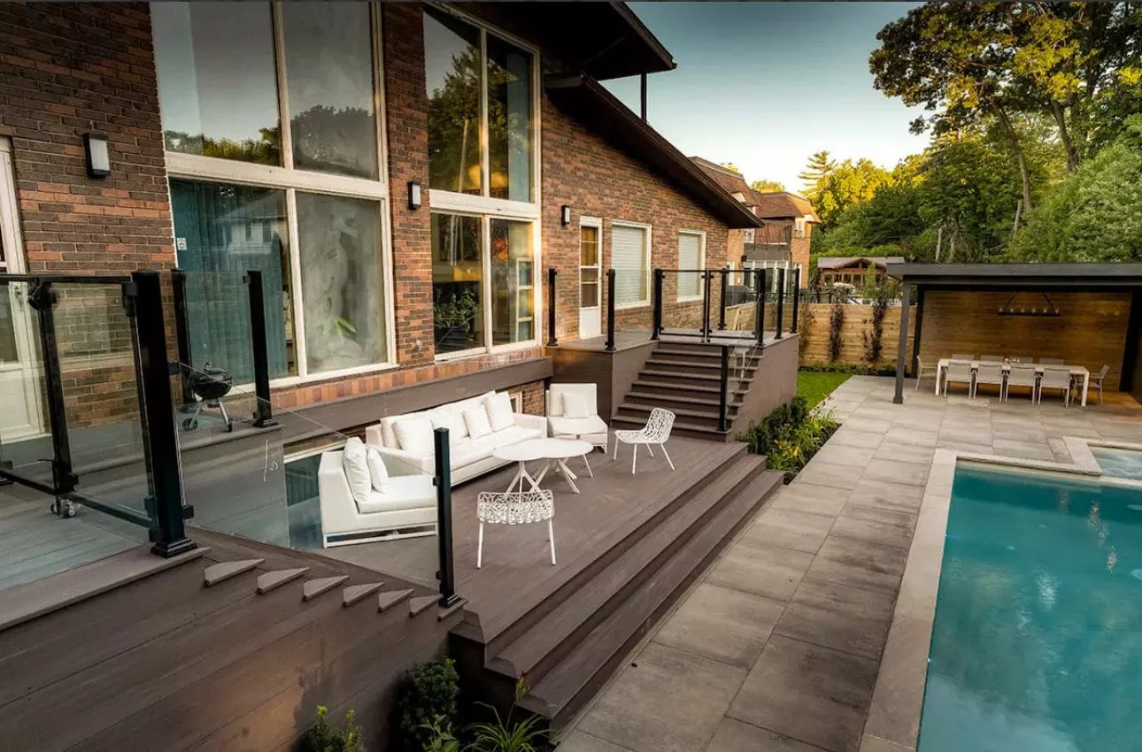 Multi-level deck with glass railings overlooking a pool and cabana at twilight