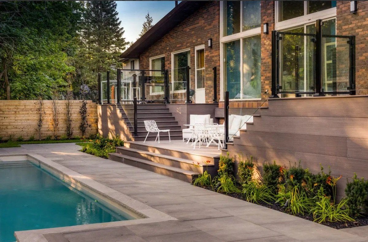Composite deck with tiered steps and glass railing beside an in-ground pool at dusk
