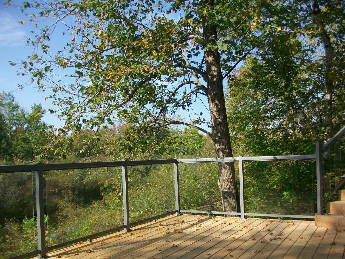 Cedar deck with glass railing overlooking a wooded river in autumn light