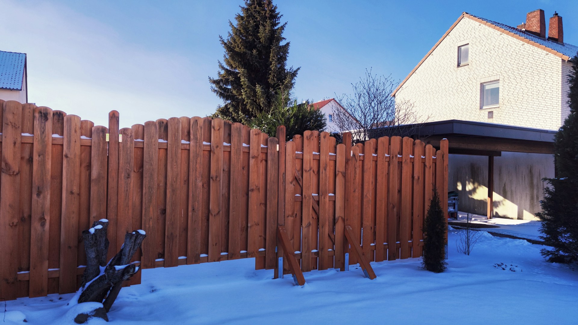 Board-on-board wood fence in fresh snow, with two diagonal braces propping up one section