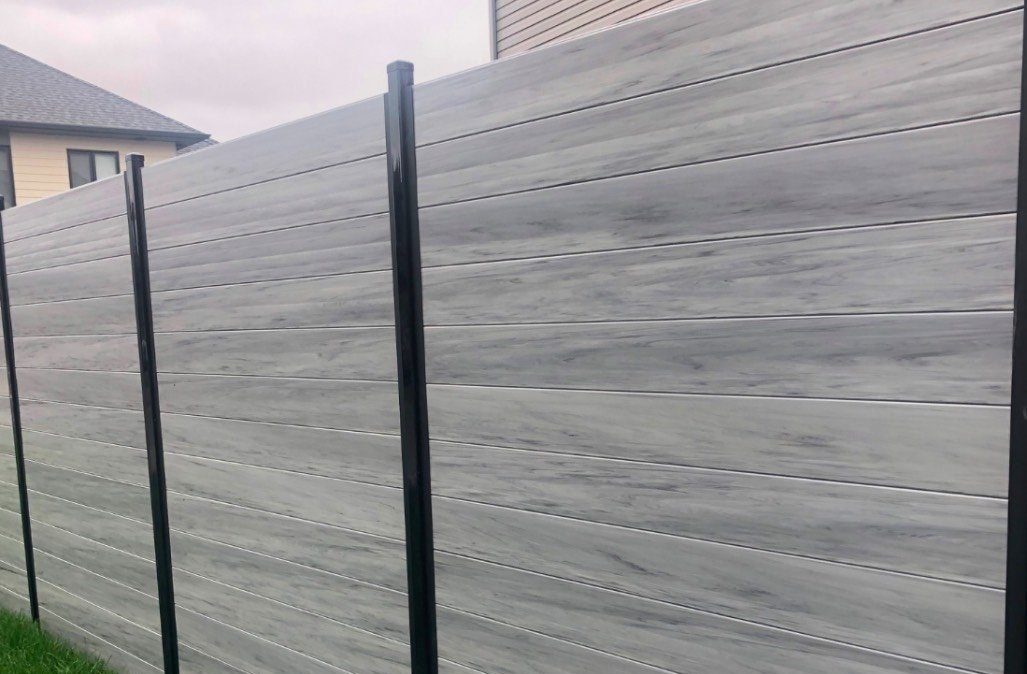 Grey woodgrain composite privacy fence with black posts running along a fresh lawn beside an Ottawa home