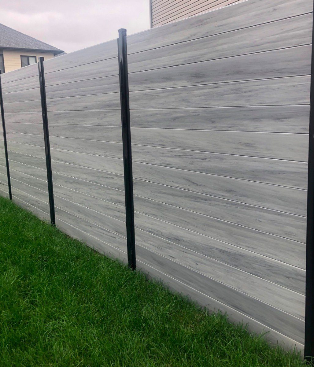 Grey woodgrain composite privacy fence with black posts beside a fresh lawn