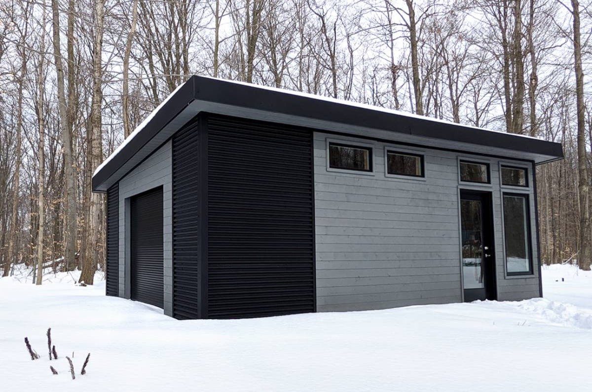 Modern black-and-grey detached garage in a snowy wooded lot