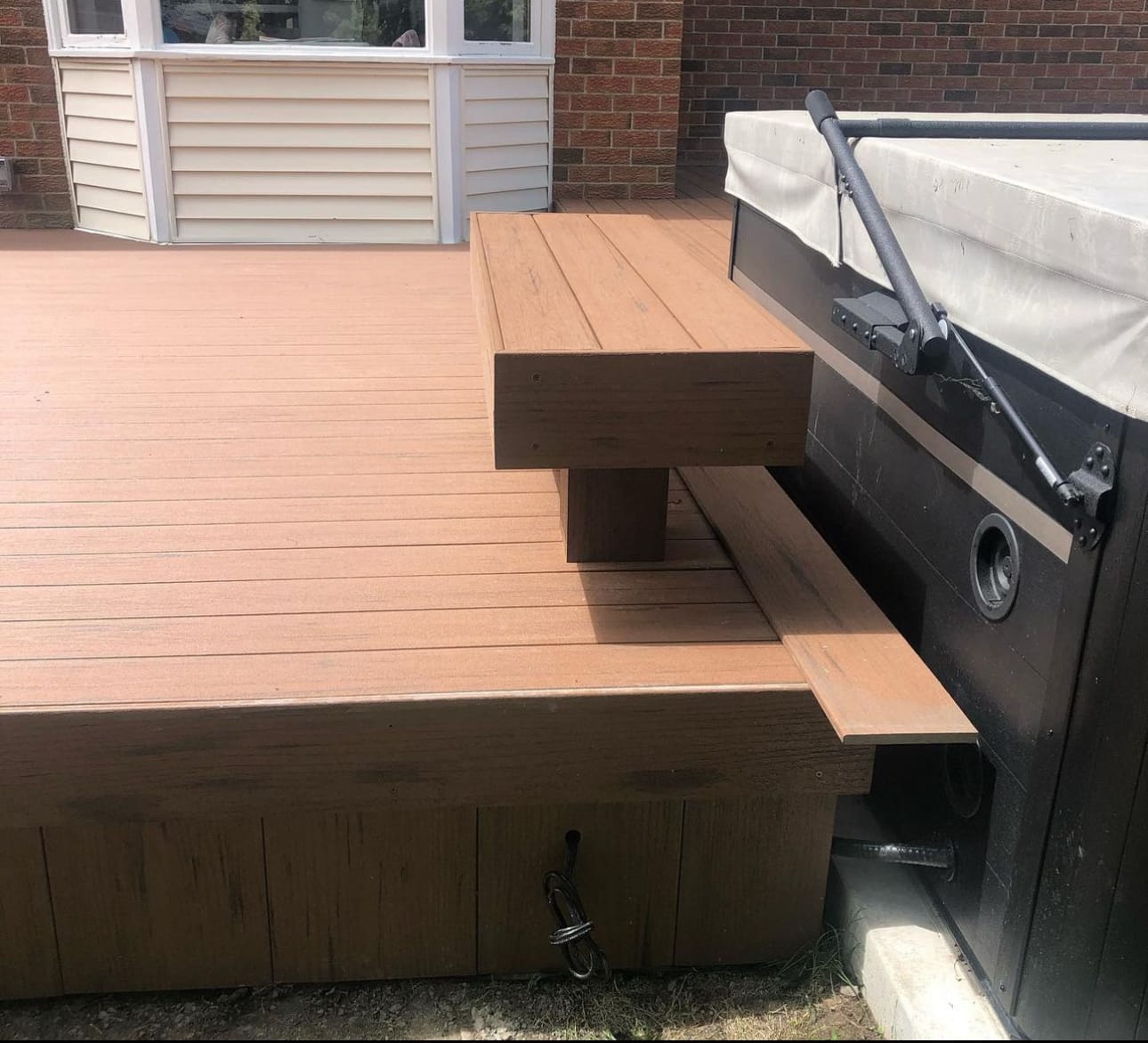 Close-up of a brown deck built around a hot tub, with a raised step beside the tub
