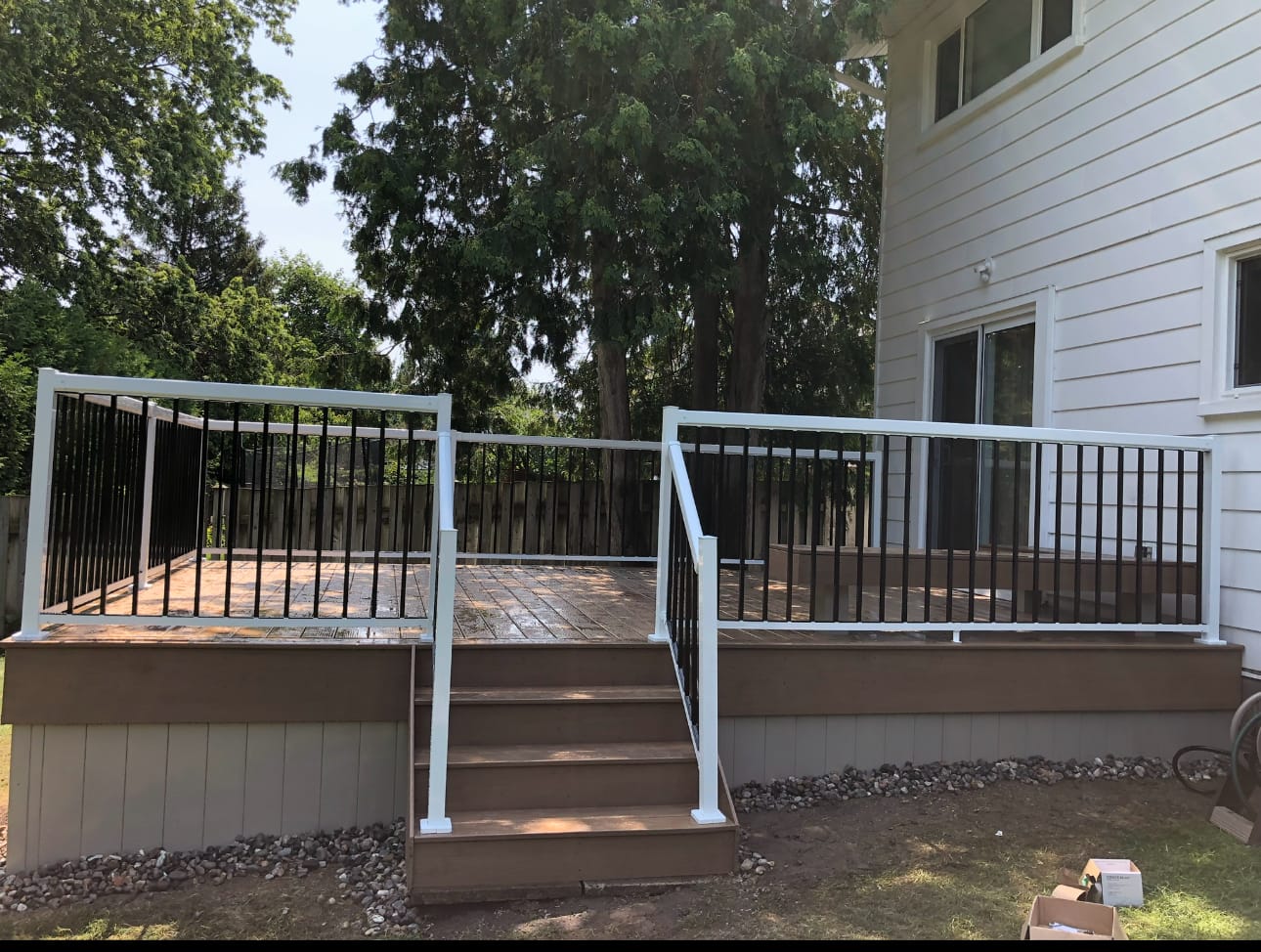 Brown deck with white-framed black railings and a short stair, beside a house with white siding