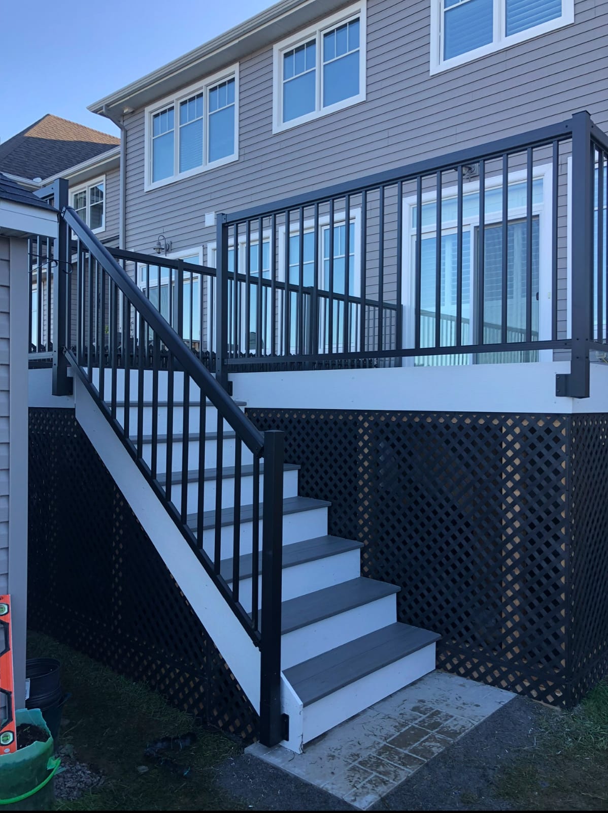 Raised deck with black metal railings, white stairs with grey treads and black lattice skirting