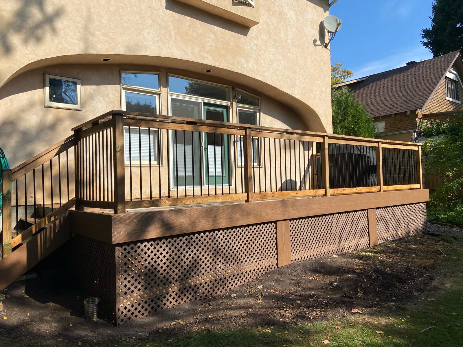 Long brown deck with a wood railing, black balusters and lattice skirting along a stucco house