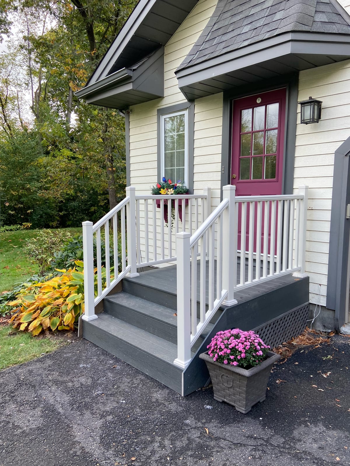 Small front porch with grey steps, white railings and lattice skirting at a red front door
