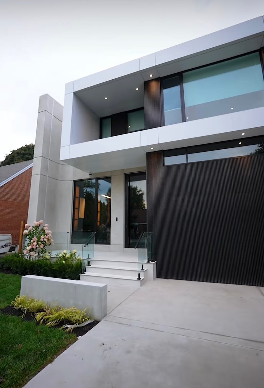 Front steps with a glass railing at a modern house with white panels and dark vertical cladding