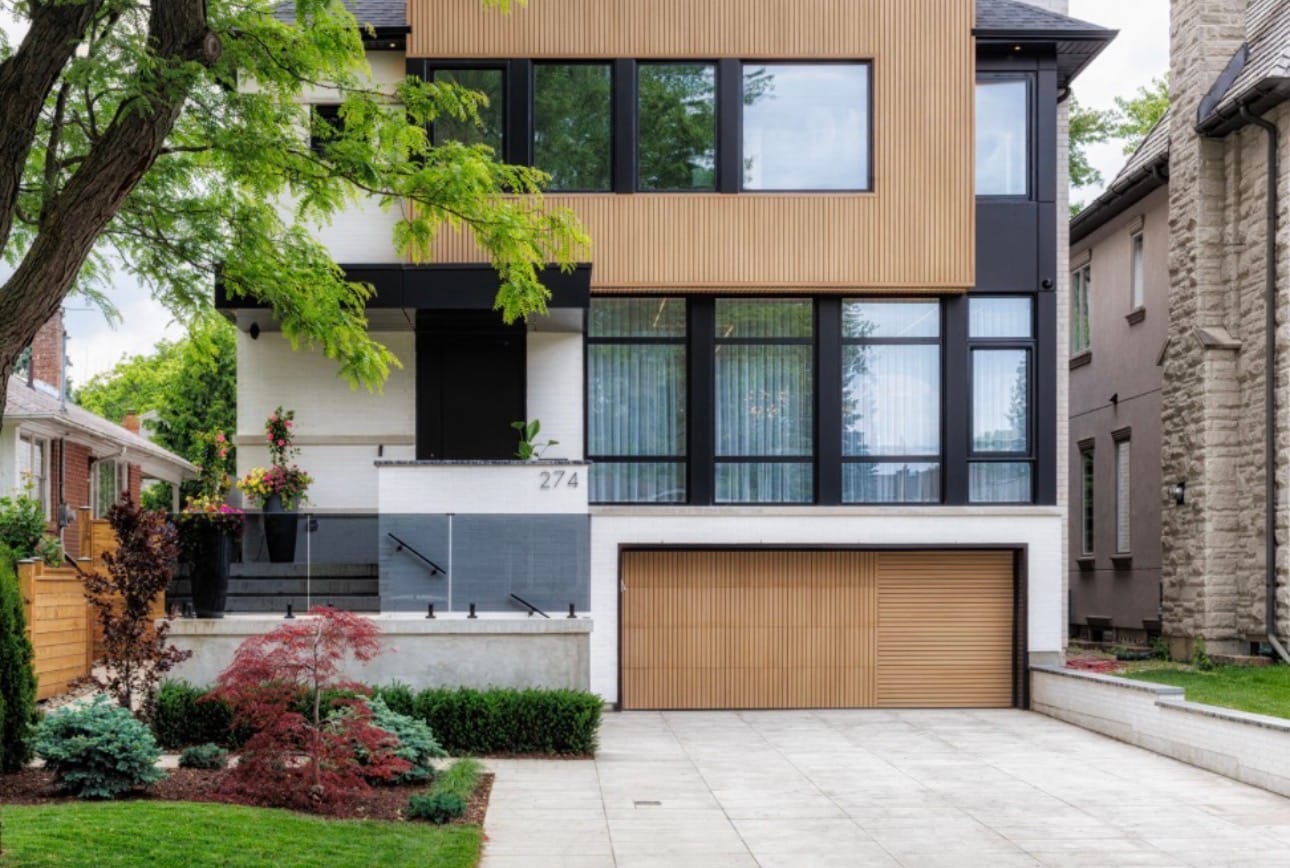 Large-format paver driveway at the front of a modern house, with planted beds and a glass railing on the front landing