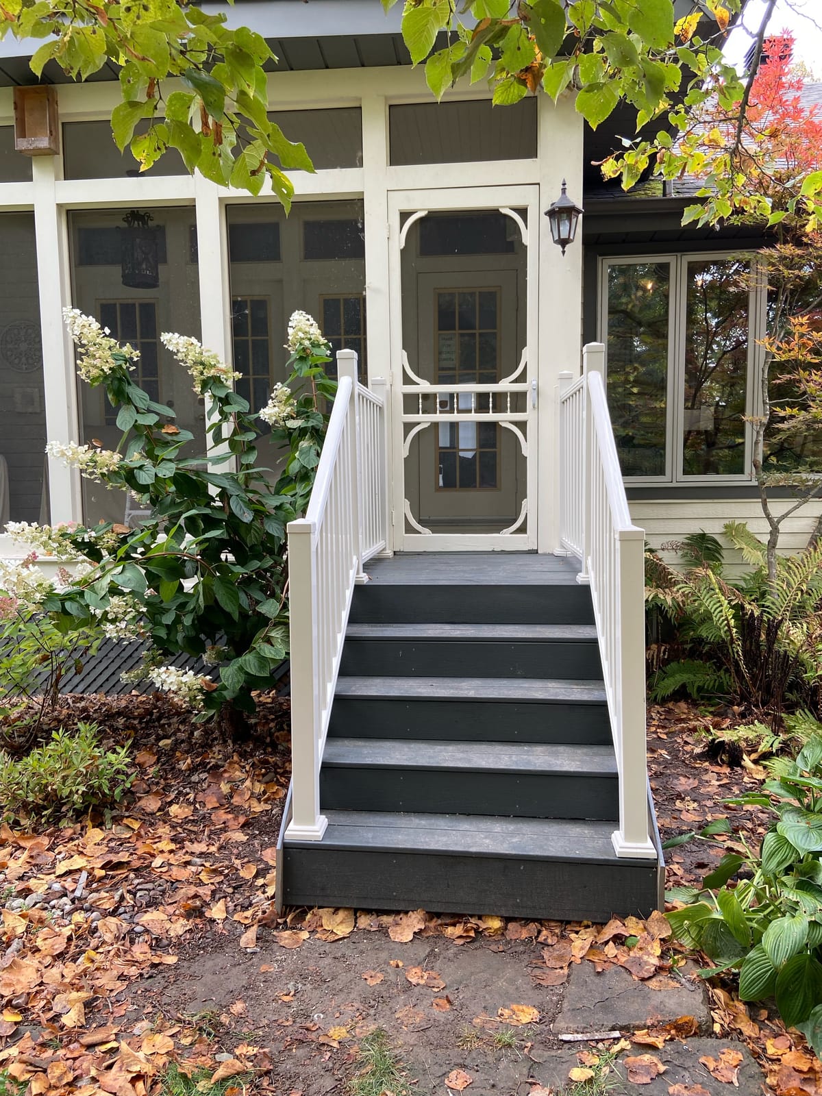 Front stairs with dark grey treads and white railings up to a screened porch door, with fallen leaves around them