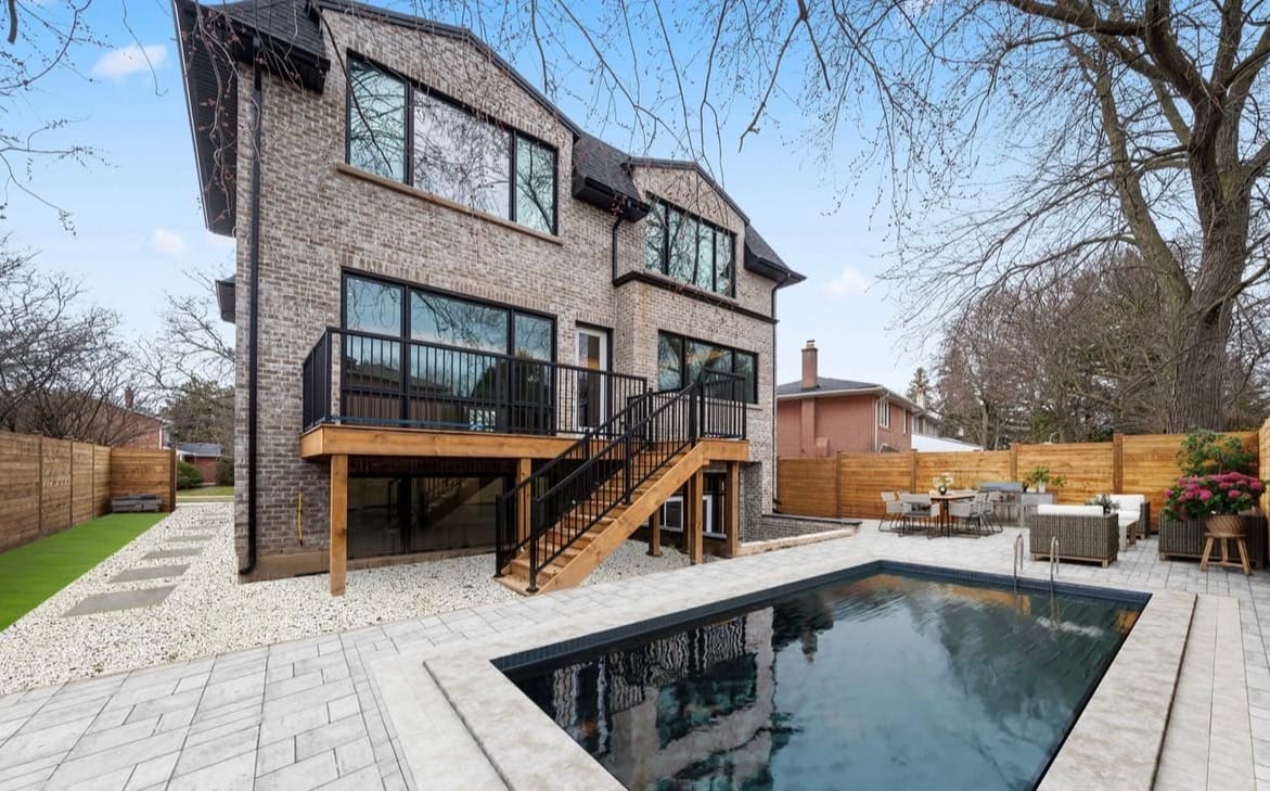 Raised rear deck with black metal railings and wood stairs down to a paver pool patio, beside a horizontal wood privacy fence