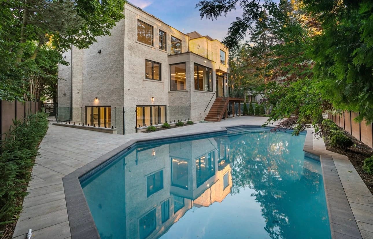 Pool edged with large stone pavers alongside a brick house, with stairs up to a raised deck