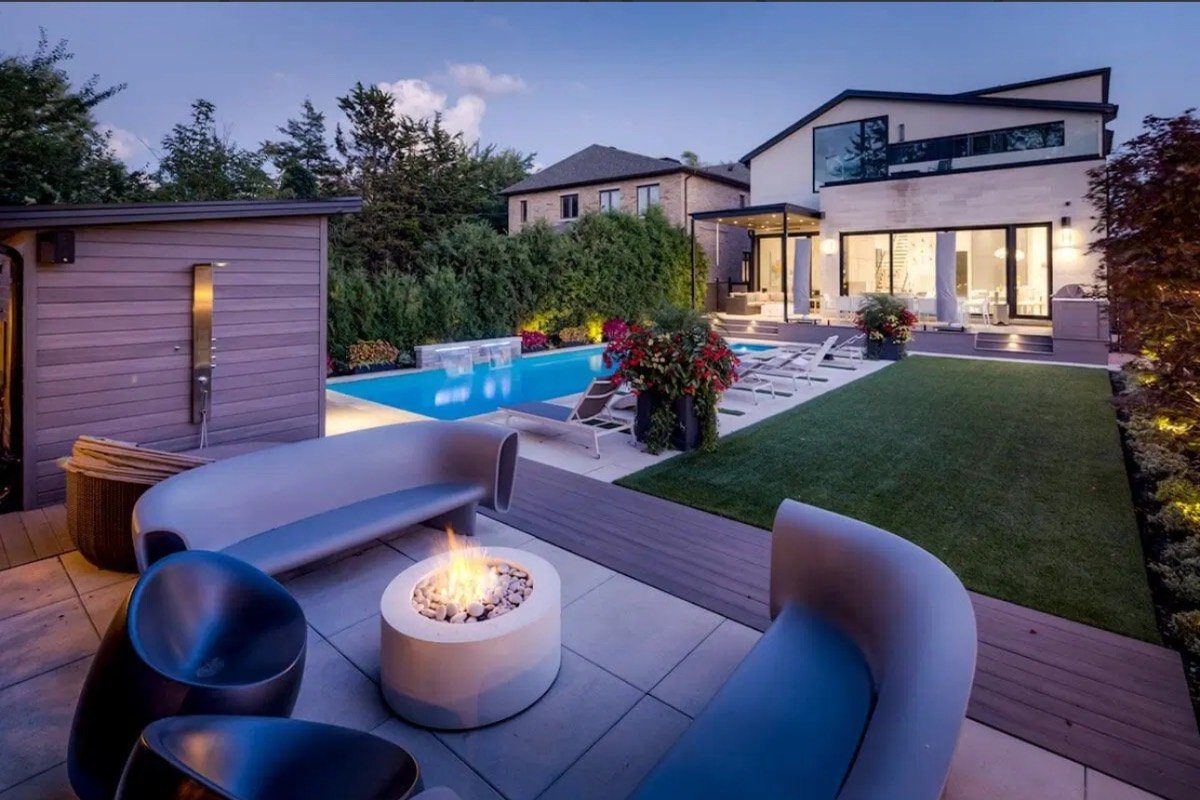 Twilight backyard with a fire pit lounge, pool, turf and paver patio beside a modern home