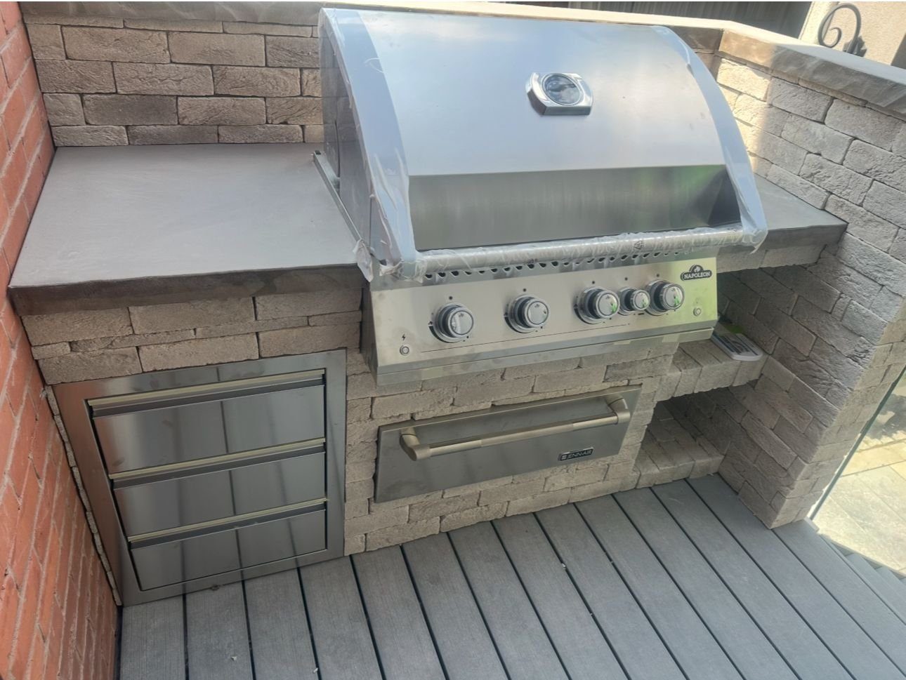 Stone outdoor kitchen with a built-in grill and drawers on a composite deck