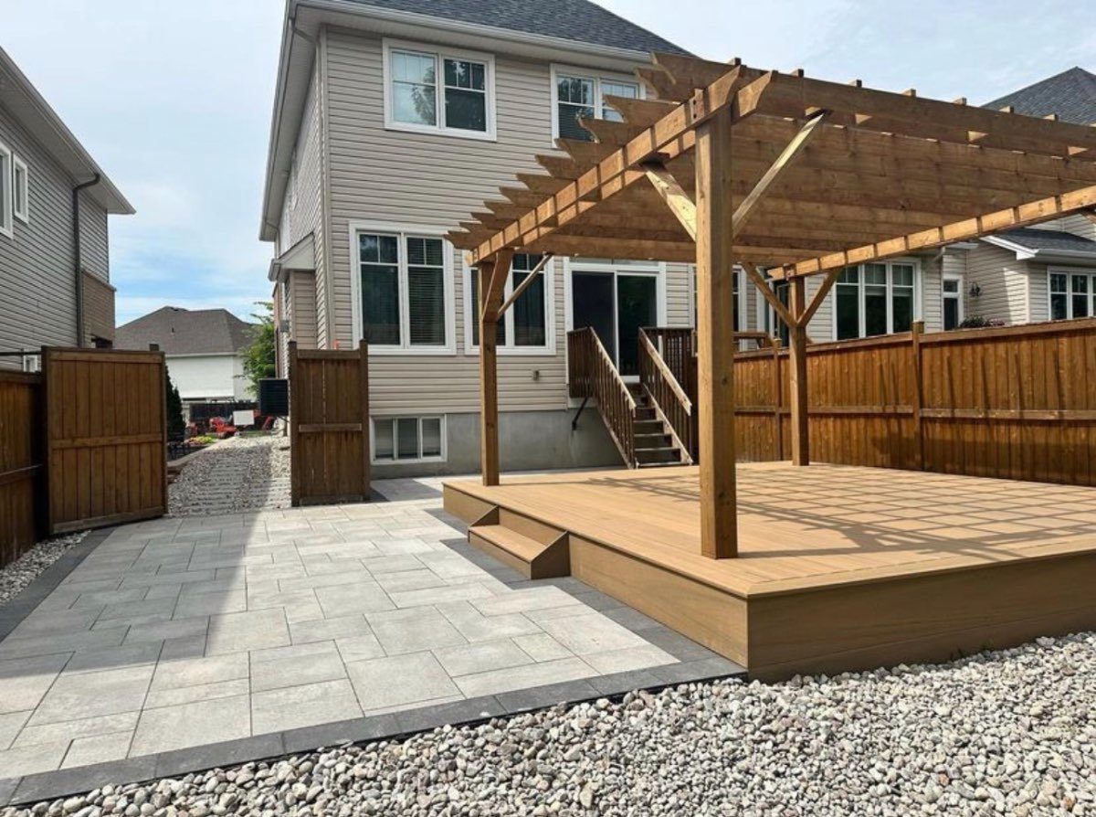 Wood pergola over a composite deck with a paver patio behind a home